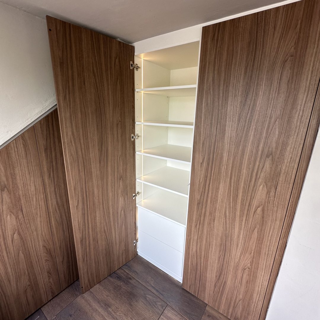 Maatwerk kledingkast in Hoevelaken onder een schuin dak met houten deuren, wit interieur, schappen en geïntegreerde verticale LED-verlichting.
