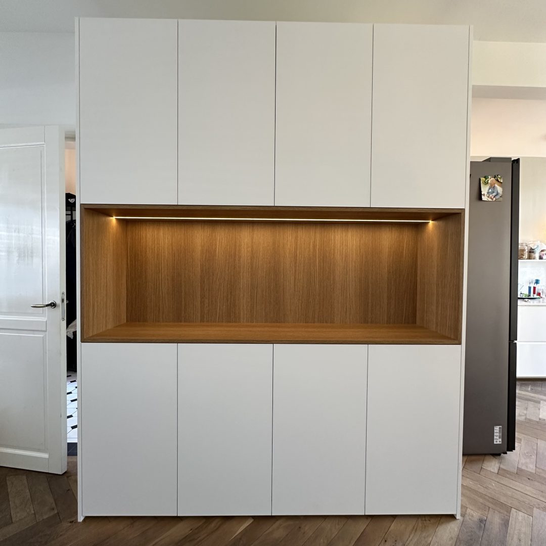 Witte maatwerkkast met een eikenhouten open nis voorzien van led-verlichting op een visgraatvloer in een modern interieur.