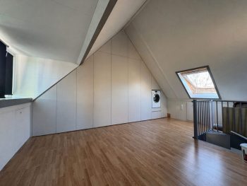 Grote witte inbouwkast op maat onder een schuine wand op zolder met een ingebouwde wasmachine